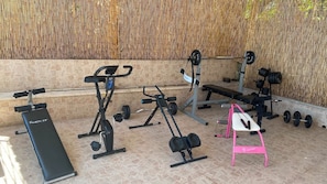 A gym with various exercise equipment including a bench, weight bench, and dumbbells.