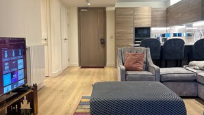A modern living room with a flat-screen TV, a sofa, an ottoman, and a colorful striped rug. - Cozy Riverview London Apartment Near the o2 Arena (London)