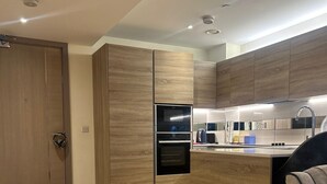 A modern kitchen with wooden cabinets, a built-in oven, and a countertop with a sink and kettle. - Cozy Riverview London Apartment Near the o2 Arena (London)