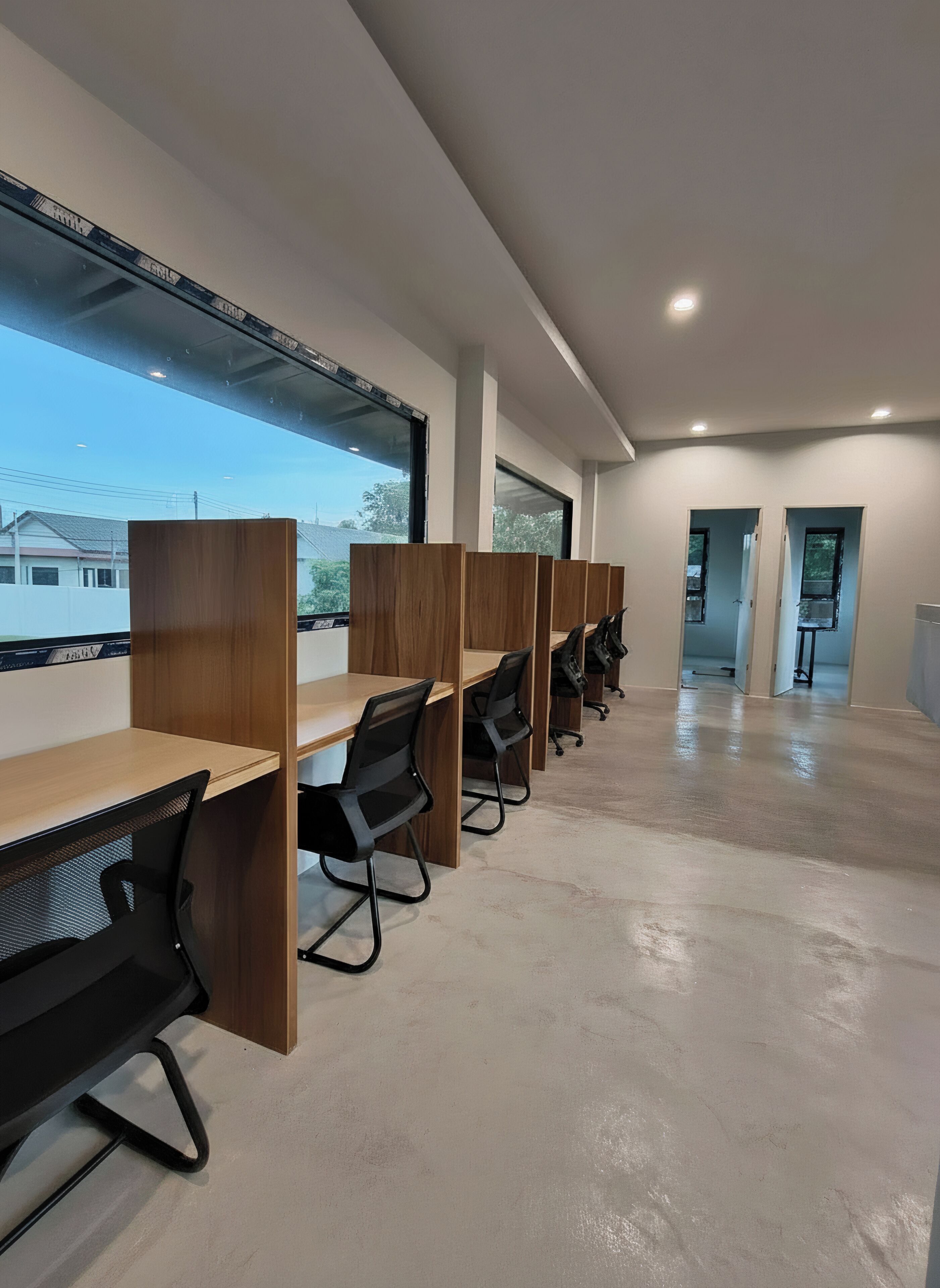 Un espacio de oficina moderno con escritorios de madera largos y sillas de oficina negras, ventanas grandes y suelo de hormigón.
