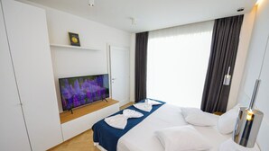 Ett hotellrum med en säng, en tv som är monterad på väggen, en dörr och ett fönster med gardiner.