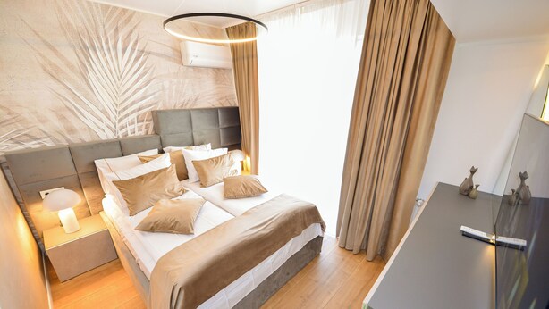 A modern bedroom with a bed, bedside tables, a nightstand, a dresser, and a large window with curtains.