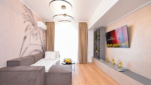 A modern living room with a sectional sofa, a flat-screen TV mounted on the wall, and a small side table with decorative items.