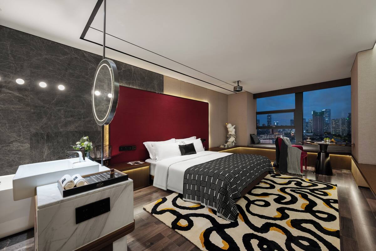 Een moderne hotelkamer met een groot bed, een zithoek met uitzicht op de stad, een badkamer met ligbad en een groot raam.
