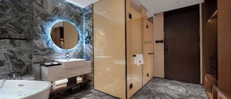 A modern bathroom with a marble wall, a round mirror, a freestanding bathtub, and a wooden vanity.