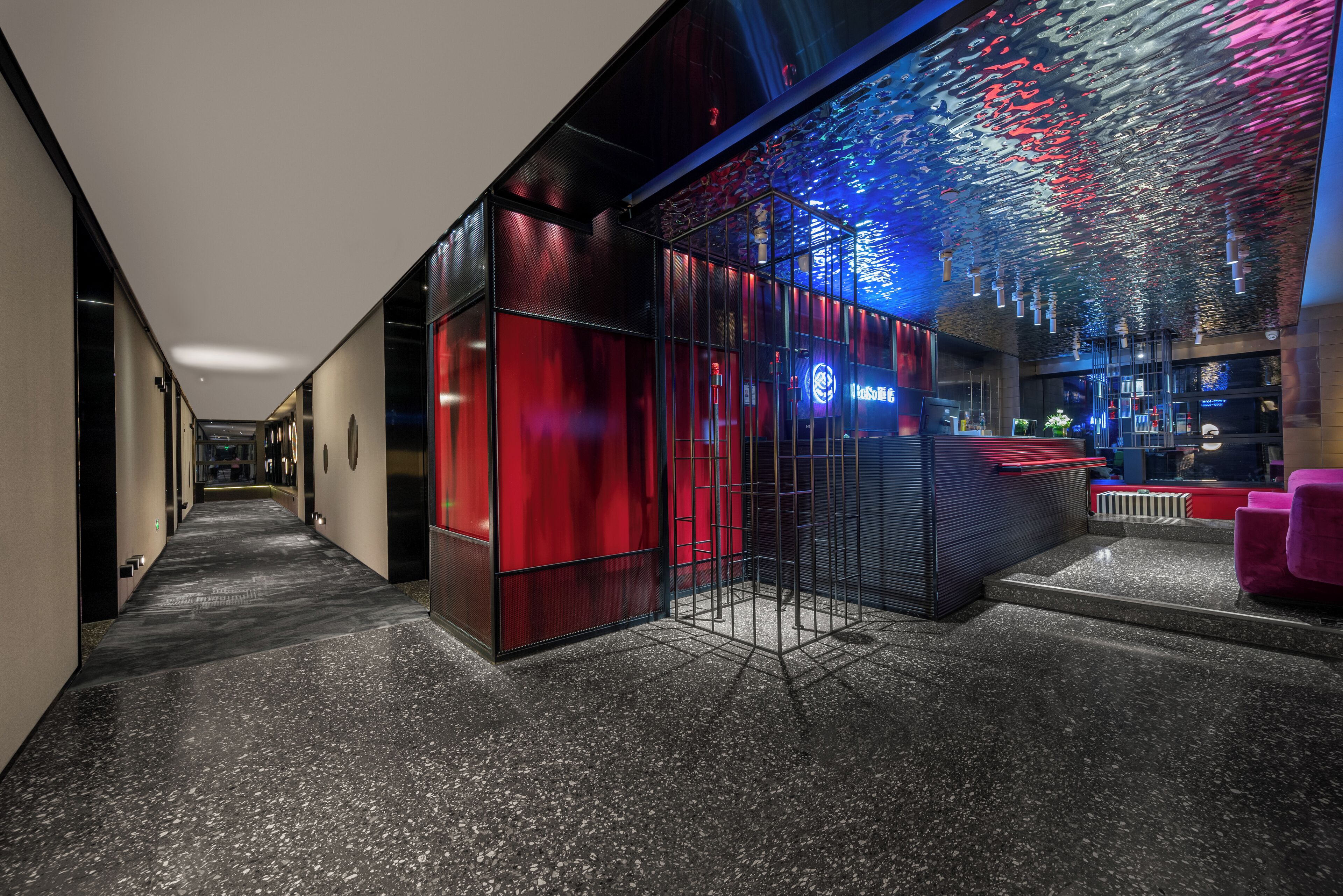 Een moderne hotellobby met een spiegelende glazen wand, een receptiebalie en een zithoek.