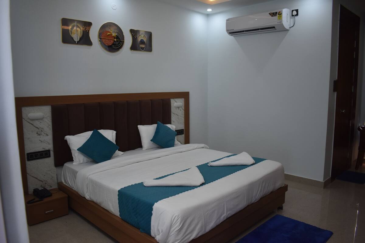 A neatly made bed with white and teal bedding, a wooden headboard, and a wall-mounted air conditioner.