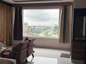 A room with a large window, a sofa, a wooden wardrobe, and a television.