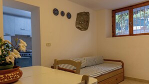 Ett kompakt bostadsutrymme med ett litet kök, en säng med randigt sänglinne, ett matbord med en stol och dekorativa tallrikar på väggen.