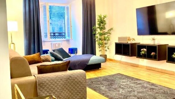 Uma sala de estar moderna com um sofá, uma mesa de centro, uma televisão e uma janela grande com cortinas.