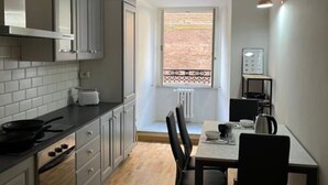 Cozinha compacta com armários cinzas, bancada preta e janela com vista para uma parede de tijolos.