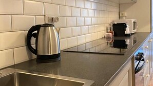 Cozinha com painel de azulejos brancos, chaleira de aço inoxidável e eletrodomésticos modernos.