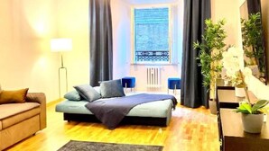 Quarto com cama, sofá, escrivaninha e janela com cortinas.