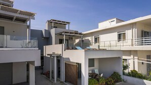 Un immeuble résidentiel moderne à plusieurs étages, doté de balcons, d’un espace extérieur aménagé pour s’asseoir et d’une cour intérieure recouverte de gravier.