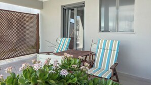 Un espace patio avec une table et deux chaises à rayures, une clôture en bois et une fenêtre donnant sur un beau paysage.