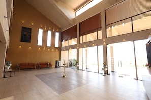 Un hall d’entrée spacieux avec un plafond haut, de grandes fenêtres et un coin salon avec des canapés.