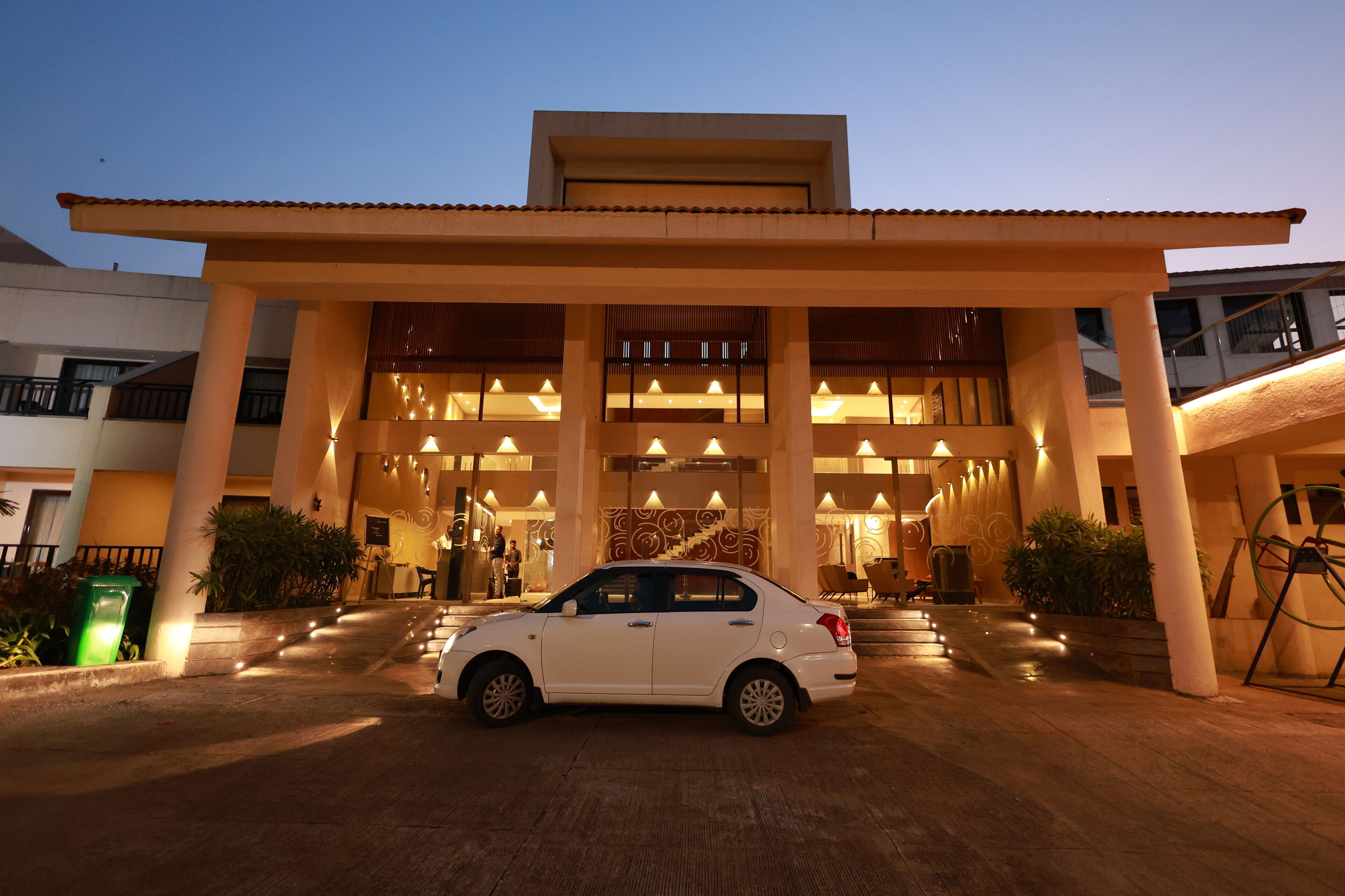 A white car parked in front of a building with a large entrance and multiple columns.