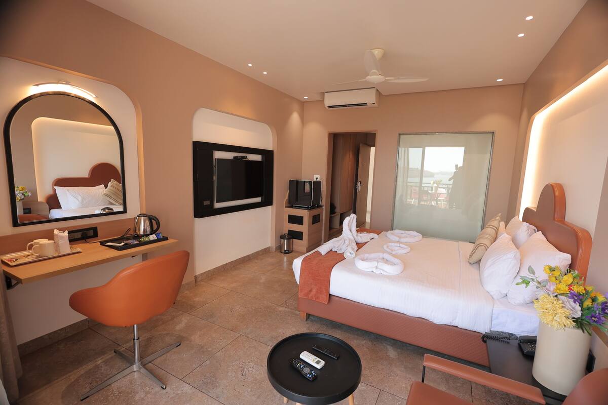 A hotel room with a bed, a desk with a chair, a television, and a large mirror.