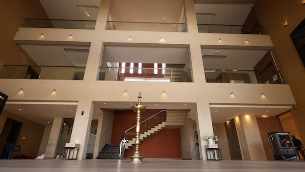 Un interior de varios niveles con una escalera central, barandillas de vidrio y un objeto decorativo de latón.