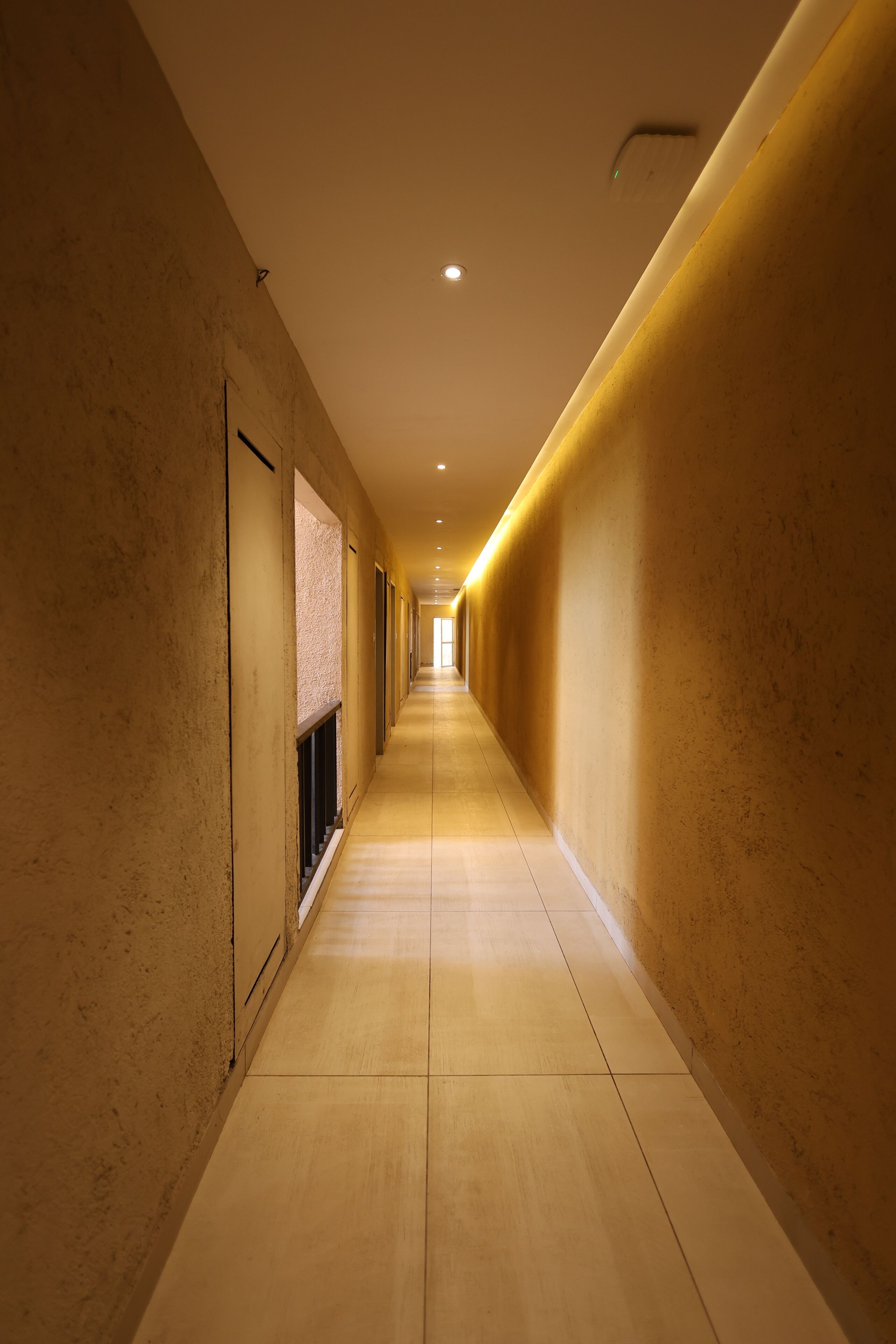A long, narrow hallway with a consistent wall texture and a tiled floor, leading to a bright end point.