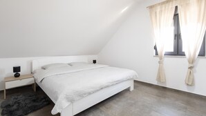 A bedroom with a bed, a nightstand, a lamp, a rug, and a window with curtains. - Luxurious home in Vukovar (Vukovar)