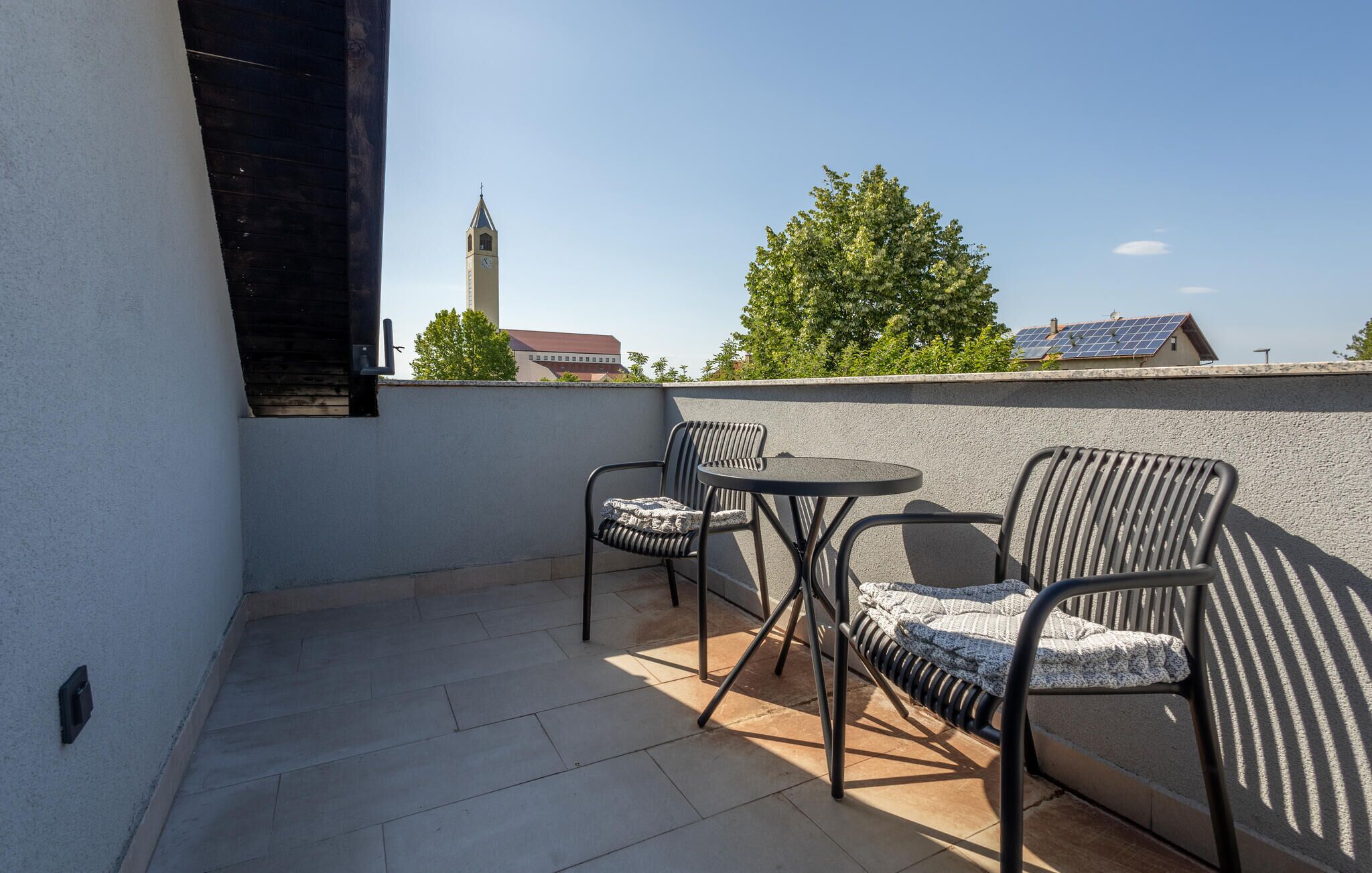 Ein Balkon mit zwei Stühlen und einem kleinen Tisch, mit Blick auf eine Stadtlandschaft mit einem Glockenturm.