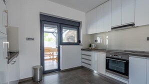 A modern kitchen with white cabinets, a stainless steel oven, and a window overlooking a patio area. - Luxurious home in Vukovar (Vukovar)