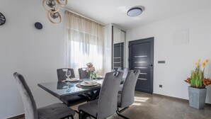 A modern dining area with a glass table, grey upholstered chairs, and a vase with flowers. - Luxurious home in Vukovar (Vukovar)