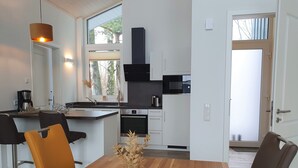 Una cocina moderna con armarios blancos, un microondas negro y un horno empotrado. Hay una mesa de comedor con sillas y un jarrón con flores secas.