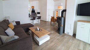 Una sala de estar moderna con sofá, mesa de centro y televisor. Cuenta con una zona de cocina con mesa y sillas.