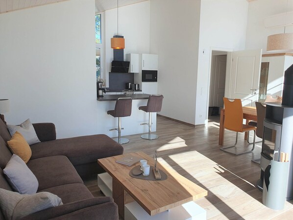 A modern living space with a sofa, a wooden coffee table, a kitchen area with a dining table and chairs, and a fireplace.