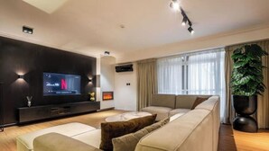 En moderne stue med et stort fladskærms-tv, en pejs, en sofa og en stor stueplante.