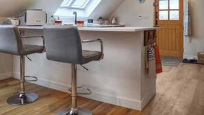 A modern kitchen with a skylight, two bar stools, a wooden door, and a clock on the wall. - 1 bedroom accommodation in near Uppingham (near Uppingham)