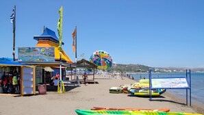 Una playa con un quiosco, un parasail colorido y varias kayaks.