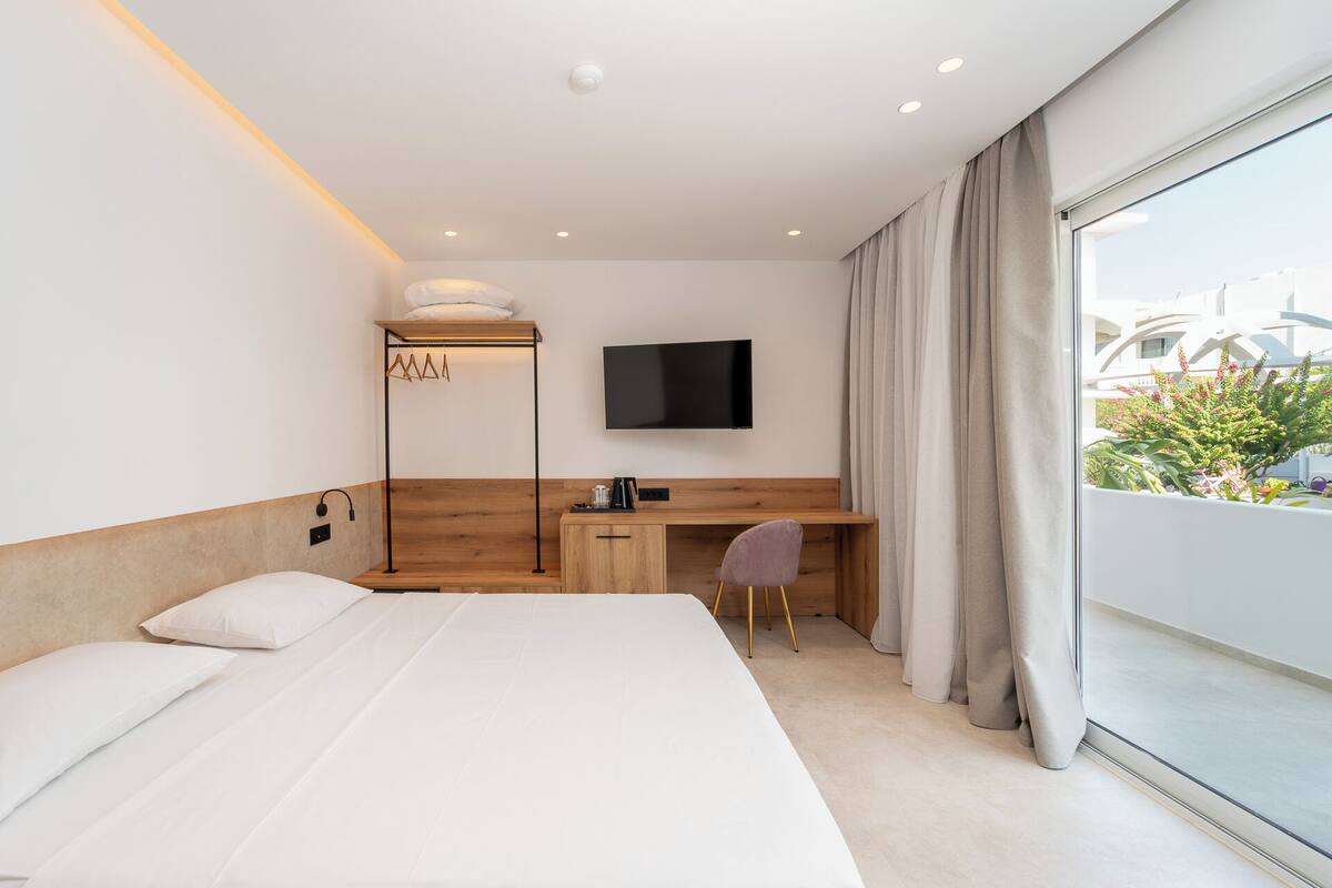 Habitación de hotel moderna con una cama grande, un escritorio, una silla, un televisor y vistas a zonas verdes.