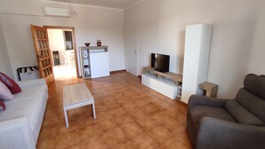 A living room with a sofa, a grey armchair, a coffee table, a TV on a wooden stand, and a kitchen area with a fridge and a microwave. - Accommodation near Assisi. Located in the countryside for a relaxing stay (Tordandrea di Assisi)