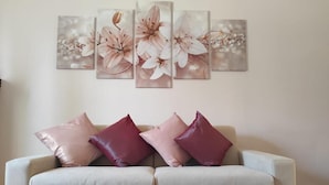 A living room with a light-colored sofa, three cushions, and a wooden coffee table. A floral artwork is displayed above the sofa. - Accommodation near Assisi. Located in the countryside for a relaxing stay (Tordandrea di Assisi)
