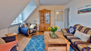 A cozy living room with a wooden table, patterned sofas, a cabinet, and a view of the outdoors. - Cozy vacation apartment Godewind directly on the dike (Dagebüll)