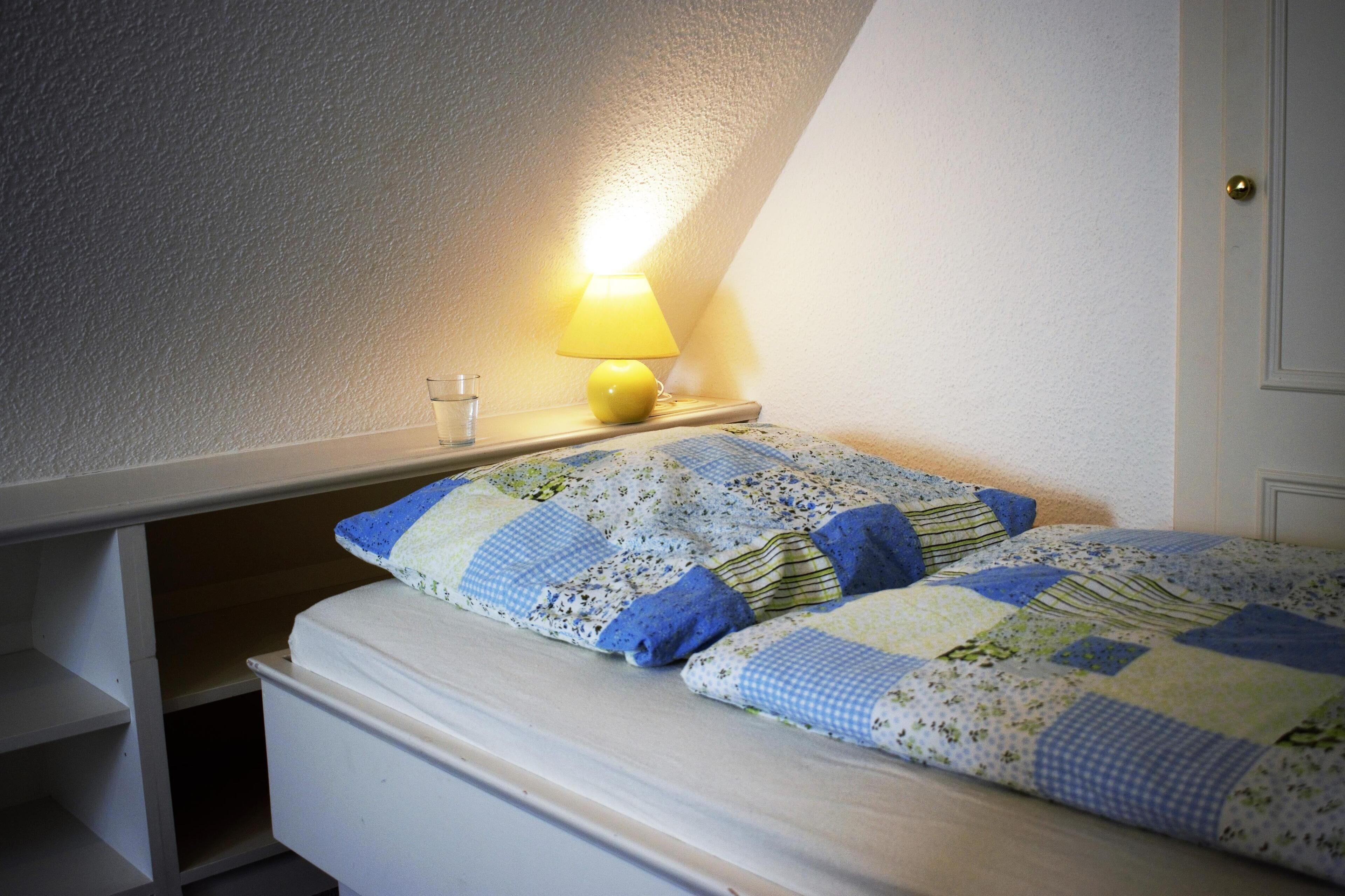 Une chambre à coucher avec un lit, une table de chevet, une lampe et une fenêtre.