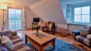 A cozy living room with a sloped ceiling, a wooden coffee table, patterned sofas, a chair, and a television. - Cozy vacation apartment Godewind directly on the dike (Dagebüll)