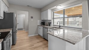A modern kitchen with granite countertops, stainless steel appliances, and a large window with blinds. - DFW Retreat • Pool, Spa & Minutes to Dallas & Fort Worth (Flower Mound)