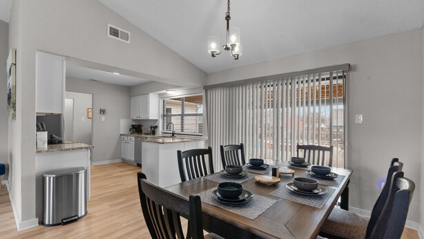 A modern kitchen with white cabinets, a stainless steel trash can, and a dining area with a wooden table set for six. - DFW Retreat • Pool, Spa & Minutes to Dallas & Fort Worth (Flower Mound)