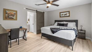 A bedroom with a bed, desk, chair, ceiling fan, and artwork on the walls. - DFW Retreat • Pool, Spa & Minutes to Dallas & Fort Worth (Flower Mound)