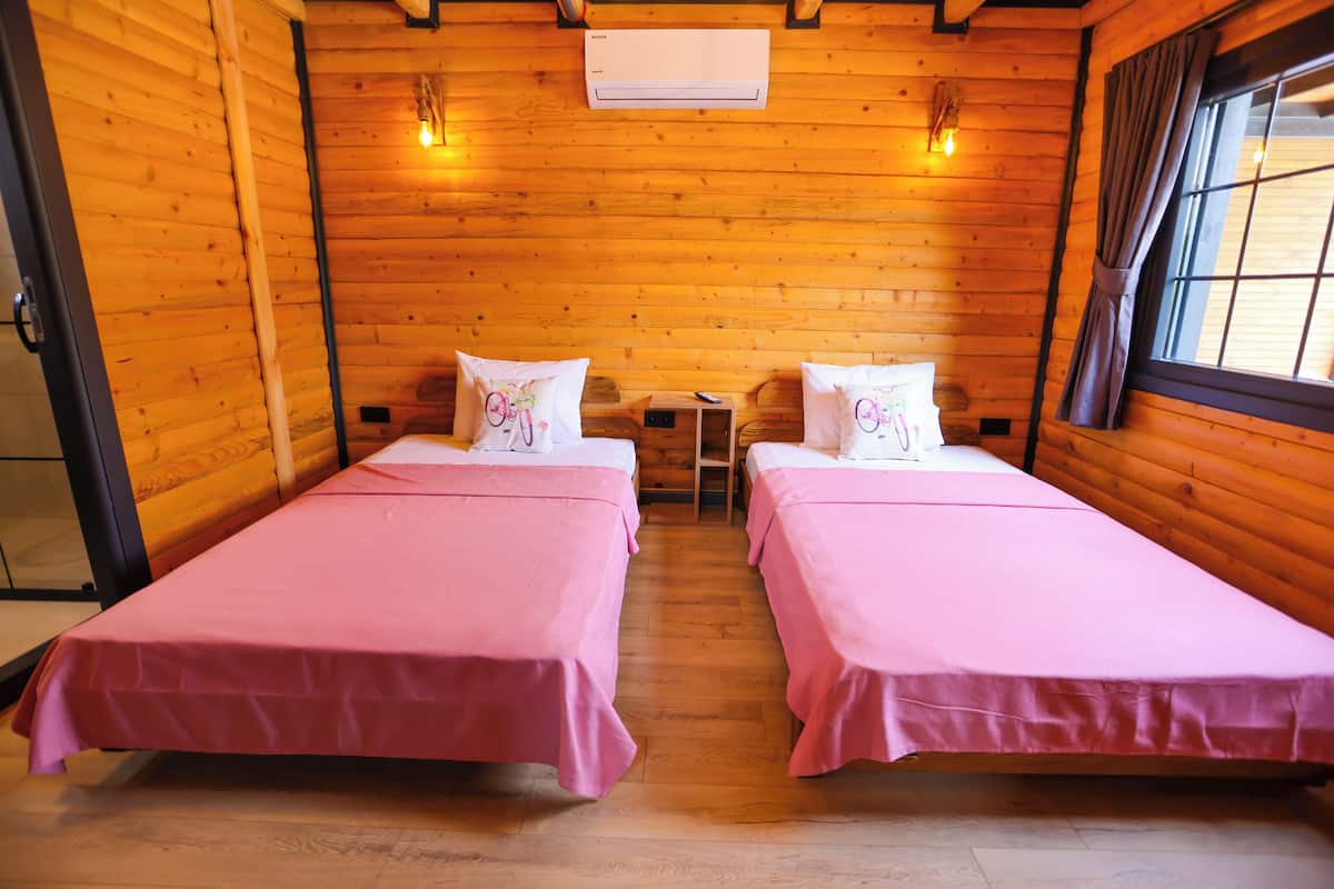 A wooden cabin room with two beds, a small table, and a window with curtains.