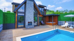 A modern house with a swimming pool, wooden deck, and a stone fireplace.