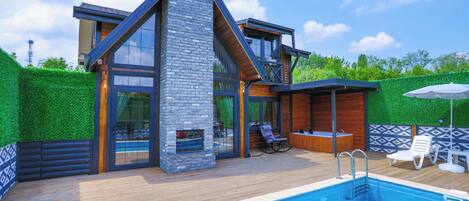 Una casa moderna con piscina, terraza de madera y chimenea de piedra.