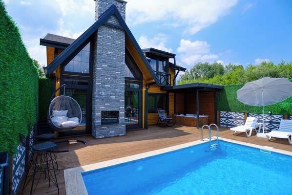 Una casa moderna con piscina, terraza de madera y mobiliario exterior.