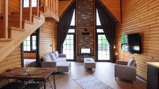 A spacious log cabin interior with a fireplace, a TV mounted on the wall, and a staircase leading to an upper level.