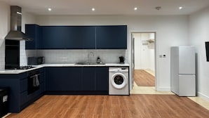 A modern kitchen with dark blue cabinets, a built-in washing machine, a microwave, and a stove.