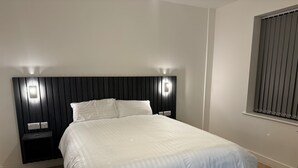 A neatly made bed with a white duvet in a modern room with a dark headboard and bedside lamps.